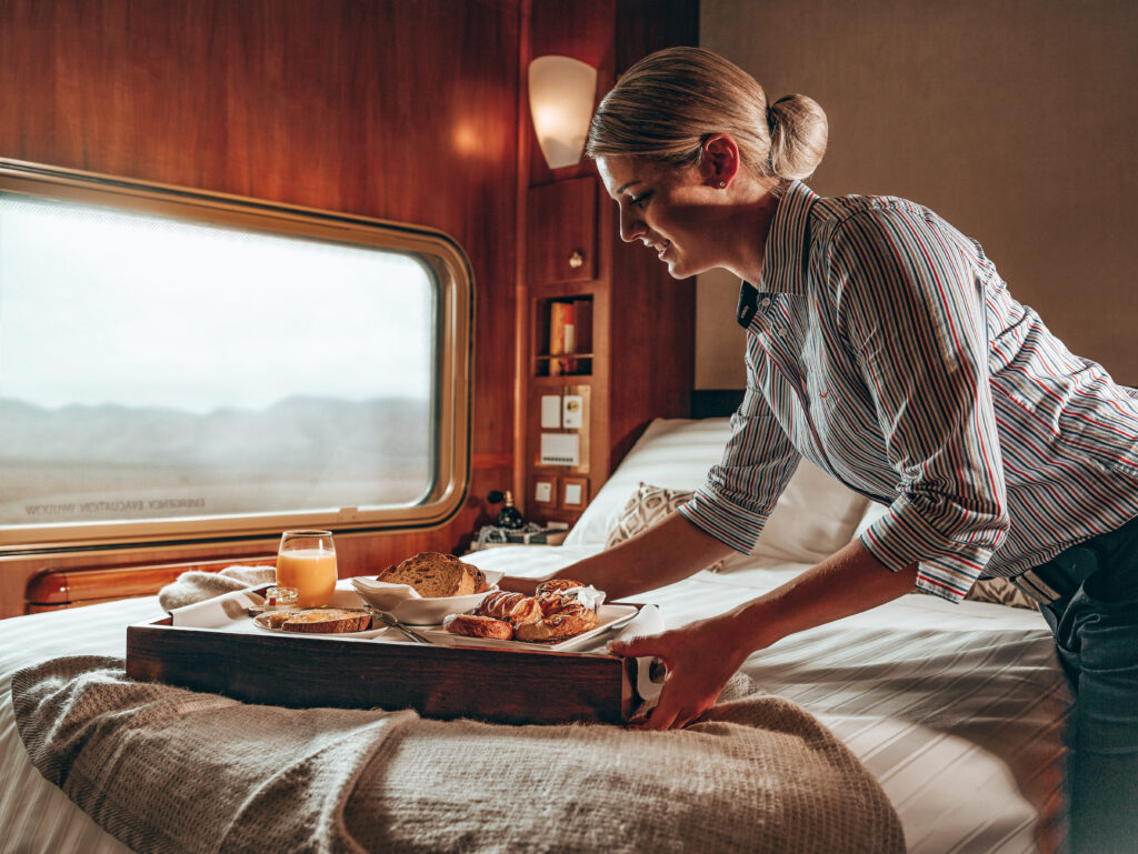 Ghan host delivering a breakfast tray in a Platinum Service cabin.