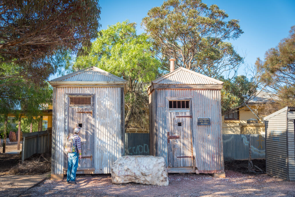 Visitor looking into historic corrugated iron jail cells in Cook, South Australia.