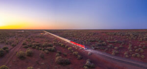 The Ghan travelling through desert terrain under a soft purple twilight sky in central Australia.
