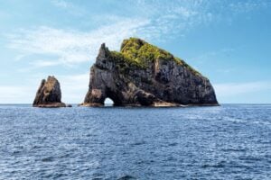 The famous Hole in the Rock sea formation rising from the ocean in New Zealand’s Bay of Islands.