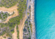 Aerial view of a winding boardwalk through coastal bushland and along rocky shores near Urunga, New South Wales.